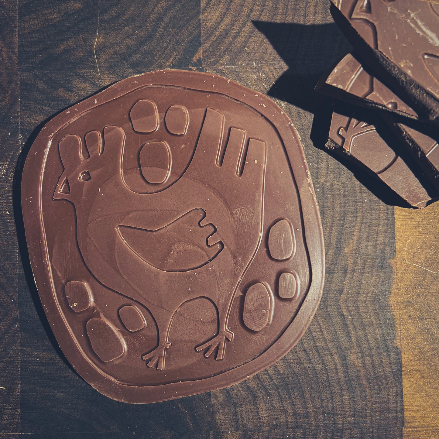 Artisan chocolate bar with hen design on a wooden background, showcasing unique craftsmanship.