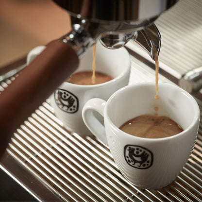Espresso pouring into two cups in a barista seminar for advanced coffee techniques.